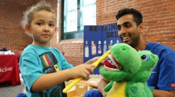A Penn Dental Student teaches a toddler how to brush teeth at the EHS Health Fair